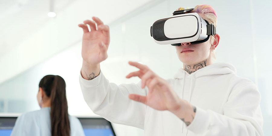 man wearing white hoodie using a VR goggles and a woman in front of a big screen in the background
