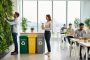 Diverse employees in a modern office participate in eco-friendly workplace initiatives, including caring for indoor plants and using reusable and recycling items.