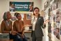 Diverse nonprofit program director and teammates in a community planning meeting, collaborating and listening around shared community materials with no readable text.